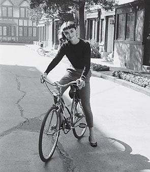 Woman on bicycle posing for photograph in front of house.