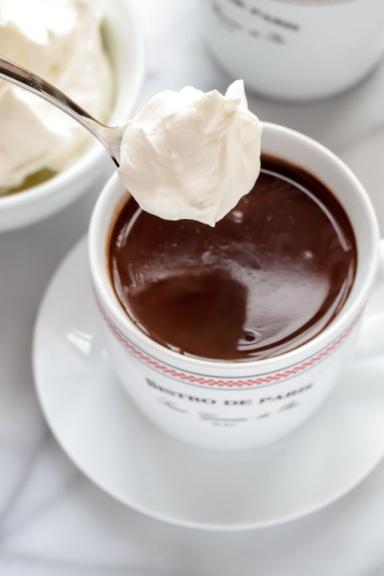 A spoon full of whipped cream over a cup of hot chocolate.
