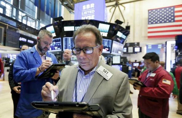A man is looking at his tablet while standing in front of the stock market.